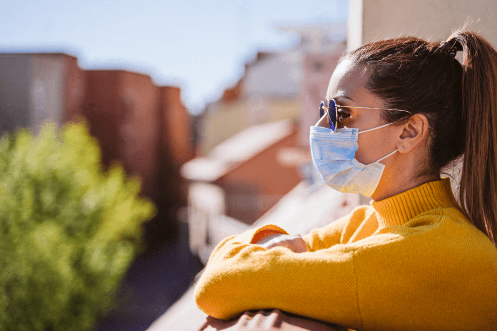 a masked woman wearing sunglasses overlooks a balcony worried about covid-19