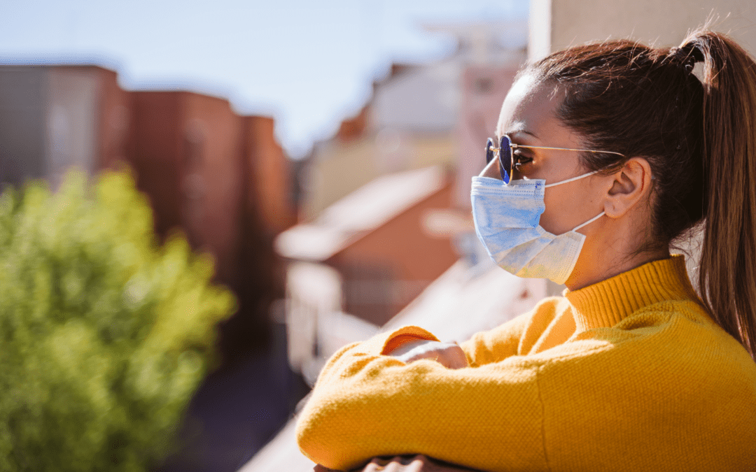 a masked woman wearing sunglasses overlooks a balcony worried about covid-19