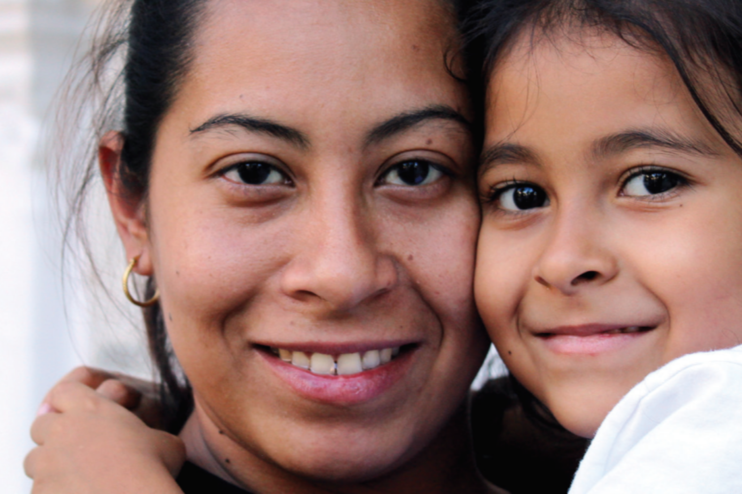 a close up of a smiling mom and daughter, cheek to cheek