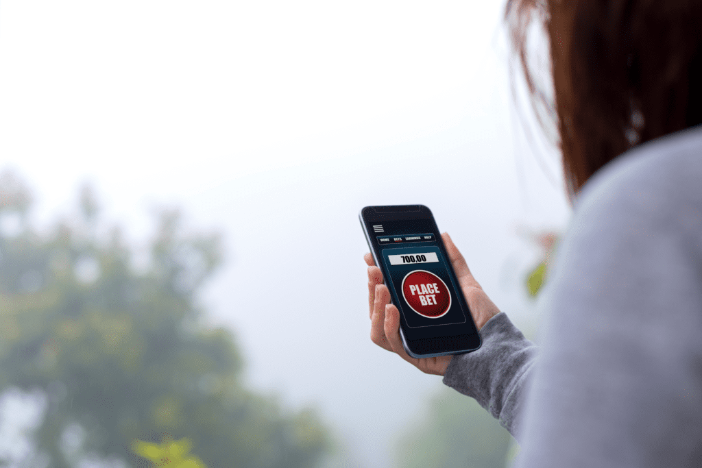 a person on a balcony holds a smartphone with a betting app opened